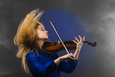 Keman çalmaya dalmış genç bir kadının büyüleyici görüntüsü. Duygularını müzikle ifade ederken saçları dinamik bir şekilde akıyor, dengesiz bir arkaplanda geçiyor..