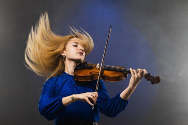 Mavi elbiseli genç bir kadının canlı bir görüntüsü, tutkuyla keman çalıyor, saçları dramatik bir şekilde etrafa yayılıyor..
