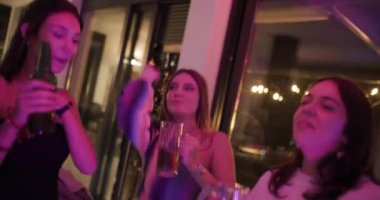 Arkadaşlar bir doğum günü partisinde içki içip dans ediyorlar. Partinin renkli ışıklandırmasıyla canlı bir atmosferi var. Kutlama havası yaratıyor..