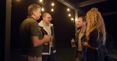 Arkadaşlar gece terasta içki içip sohbet etmekten zevk alıyorlar. Ilık aydınlatma sıcak bir atmosfer yaratır..