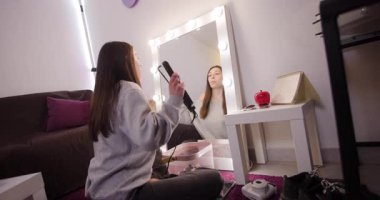 Genç bir kadın hazırlanıyor, şarkı söylüyor ve aynanın önünde saçını düzeltiyor. Eğlenceli bir gece için hazırlanıyor..