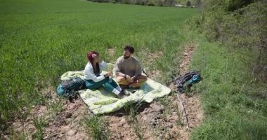 Genç bir çift yürüyüş yapmaya, sohbet etmeye ve yeşil bir tarlada piknik battaniyesinde içkiye ara veriyor..