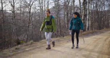 İki bayan arkadaş dağ yolunda yürüyüş yapmaktan hoşlanıyor. Sırt çantaları ve su şişeleri taşıyorlar, temiz havanın ve manzaranın tadını çıkarıyorlar..