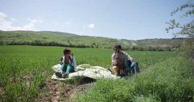 Genç bir çift güzel yeşil bir alanda rahatlatıcı bir pikniğin tadını çıkarıyor. Sırt çantalarını boşaltıp manzarayı izliyorlar..