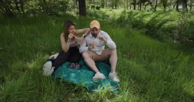 Çift, yemyeşil ve ağaçlarla çevrili bir parkta battaniyenin üzerinde piknik yapmaktan hoşlanıyor. Yemeklerinin ve birlikteliklerinin tadını çıkarırlar..