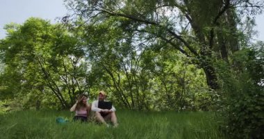 Doğada dizüstü bilgisayarda uzaktan çalışan bir çift. Kadın ve erkek parkta dizüstü bilgisayar kullanıyor. Dijital göçebeler.