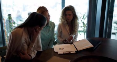 Üç iş kadını şık bir ofis ortamında önemli belgeleri incelerken odaklanmış bir tartışmaya girişiyor. Takım çalışmasında profesyonel özveri ve işbirliği sergileniyor.