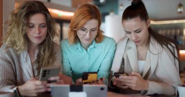 Modern bir kafede, üç iş kadını öngörülerini paylaştıkları ve girişimleri için stratejiler keşfettikleri için akıllı telefonlarına odaklanıyor. İşbirlikleri kendilerini adamış durumdalar..