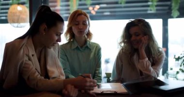 Üç kadın modern bir kafede canlı bir tartışmanın keyfini çıkarıyorlar, iletişim kuruyorlar ve birlikte gülerken fikirlerini paylaşıyorlar. Atmosfer dostane ve profesyonel, işbirliğini teşvik ediyor..