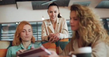 Üç iş kadını, profesyonel hedeflerini ve stratejilerini tartışmak için şık bir kafede toplandılar. Birbirlerine bakış açılarını paylaşıyorlar ve ortak bir atmosferde birbirlerine destek oluyorlar..
