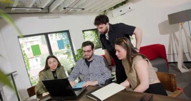 Modern bir ofisteki bir projede dört kişilik bir iş ekibi, belgeleri gözden geçirir ve dizüstü bilgisayardaki fikirleri tartışır..