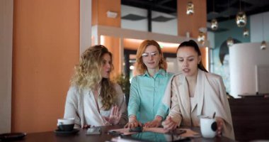 Çağdaş bir kafede üç kadın iş stratejileri üzerinde işbirliği yapıyor. Onlar kahve içerken fikir ve içgörü paylaşıyorlar..