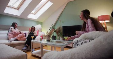 Üç arkadaş, rahat bir oturma odasında pijama giymiş, canlı sohbetlere dalmış, abur cubur ve içeceklerle kahkahalar atıyorlar, birlikte neşeli anılar yaratıyorlar..