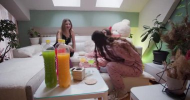 Bir grup kız evde rahat bir pijama partisinin tadını çıkarıyor, rahat bir ortamda renkli içecekler yudumlarken kahkahalar ve atıştırmalıklar paylaşıyorlar..