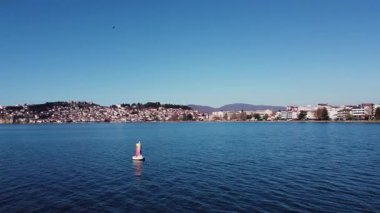 Ohri Gölü manzaralı bir martı şamandıraya tünemiş ve arka planda Ohri kenti.