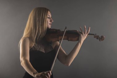 Genç bir kadının büyüleyici bir portresi. Keman çalmaya derinden odaklanmış, arka planda hafifçe aydınlatılmış, duyguları ve sanatsallığı çağrıştıran..