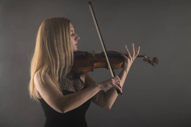 Keman çalmaya kendini kaptırmış genç bir kadının büyüleyici görüntüsü, yumuşak ışıklandırma ve sakin bir ifade..
