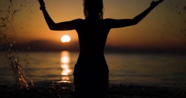 Büyüleyici bir günbatımında bir insan neşeyle suya atlar. Silüet, altın gökyüzü ile güzel bir tezat oluşturuyor, doğanın büyüleyici bir manzarası ve eğlencesi yaratıyor..