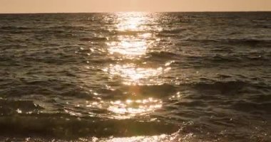 Sersemletici Altın Gün Batımı, Yumuşak Okyanus Dalgaları 'na yansıyarak, Karanlık' ta Köpüklü Su ile Sakin ve Sakin Sahil Manzarası Oluşturuyor. Ufuk, Küçük Dalgacılar Kıyı Kucağına Kadar Yumuşakça Parlıyor.