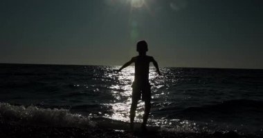 A striking silhouette of a young child celebrating freedom and hope on a tranquil beach as the sun sets over the glistening ocean waves, hands raised in triumph.