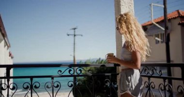 Genç bir kadın, Yunanistan 'daki güzel mavi okyanusa bakan bir otel balkonunda sabah kahvesinin keyfini çıkarıyor..