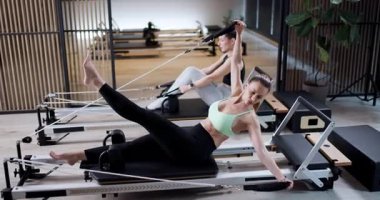 Katılımcılar, çeşitli yenilikçi egzersizler yoluyla çekirdek kuvvete ve esnekliğe odaklanan çağdaş bir stüdyoda dinamik bir pilates dersine katılıyorlar..