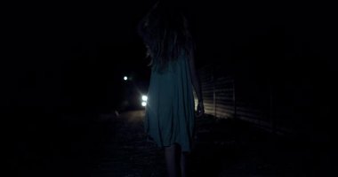 Loş bir yolda yürürken, ağaçların ve yapıların silueti bir anlığına parlayarak çevreyi aydınlatmaya ve gizemli ortamı güçlendirmeye başlar..