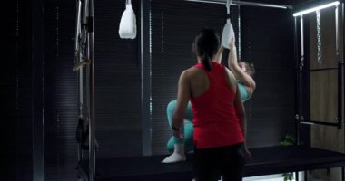 Energetic pilates workout in a stylish home studio. An instructor provides guidance as a participant engages with fitness equipment, enhancing strength and flexibility.