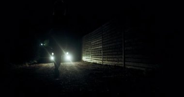 Gergin bir anda, parlak polis ışıklarından fırlayan bir kız gece etrafı çitlerle çevrili karanlık bir yolu aydınlatıyor. Hava aciliyet ve belirsizlikle dolu..