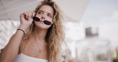 A girl relaxes at a cafe terrace, sipping her coffee and enjoying the warm sun. The vibrant atmosphere and pleasant weather enhance her moment of tranquility.