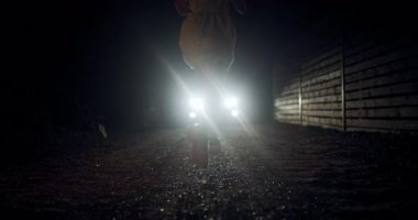 Yalnız bir koşucu çakıllı bir patika boyunca koşar, parlak farlara çarpıcı bir siluet oluşturarak karanlık çevreyi aydınlatır. Sahne, gece hareketinin özünü yakalar..