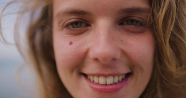 Neşeli bir kadın okyanusun kenarında dururken mutlulukla ışıldıyor. Hafif bir esinti saçlarını okşar, güneşli bir günde mükemmel bir mutluluk ve sükunet anı yakalar..