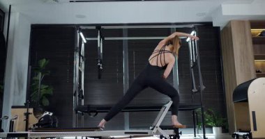 This workout features a woman practicing Pilates on a reformer, showcasing her core strength and flexibility in a contemporary studio setting with natural light.