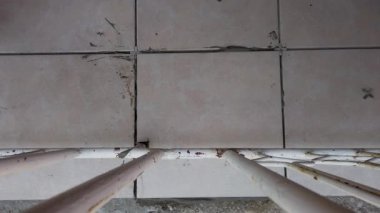 Çatlak fayanslara yakından bakıldığında döşeme ile ilgili sorunlar ortaya çıkıyor. Eldivenli bir birey, inşaat alanındaki aralıkları ve hasarı inceliyor..