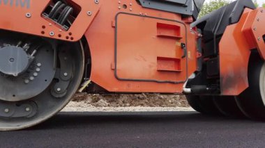 Road construction. Asphalt compactor heavy machine working on a fresh hot layer of asphalt, on a rainy day.