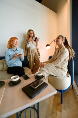 Çağdaş bir ofis alanında, üç kadın tablet kullanırken ve kahve fincanlarının keyfini çıkarırken üretken bir tartışmaya girişiyor. Rahatlamış atmosfer işbirliğini ve yaratıcılığı teşvik eder..