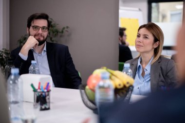 Meslektaşlar bir iş toplantısında, ofis malzemeleri ve meyvelerle çevrili takım çalışmasının ve üretkenliğin vurgulanması, olumlu bir iş ortamı sağlanması.