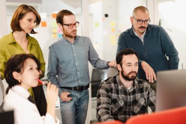 Bir grup iş adamı proje fikirlerini bilgisayarda incelerken tartışıyor. Yaratıcılık ve odaklanma ile dolu işbirlikçi bir ortamda aktif olarak yer alırlar..