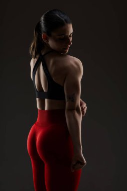 Siyah spor sutyen ve kırmızı taytlı, kaslı ve güçlü duruşunu vurgulayan fit bir kadının yan görüntüsü..