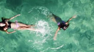 Güzel, berrak turkuaz suda yüzen iki genç kadın. Havadan yukarıdan aşağıya görünüm.