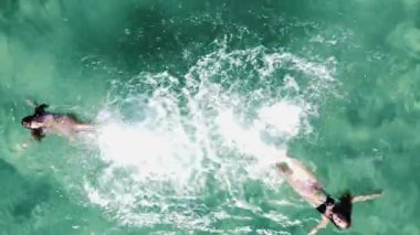Kristal berrak turkuaz suda ferahlatıcı bir yüzüşten zevk alan iki kadın. Rahatlatıcı bir yaz tatilinde dostların havadan görünüşü.