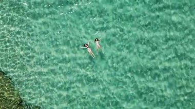 İki kadın güzel bir turkuaz tropikal okyanus suyunda yüzer ve rahatlar. Hava aracı görünümü.