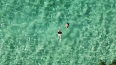 İki kadın, berrak turkuaz suyun, yüzmenin ve denizde yüzmenin tadını çıkarıyor. Yaz tatilindeki dostların havadan görünüşü.