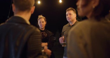 Arkadaşlar, sıradan bir akşam buluşmasının keyfini çıkarıyorlar. Sohbet ediyorlar ve sıcak sicim ışıkları altında bira içiyorlar..