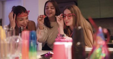 Üç genç kadın evde içki, parti hediyeleri ve kahkahalarla bir doğum günü kutlamasının tadını çıkarıyor..