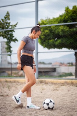 Aktif bir kadın kirli bir alanda futbol oynuyor. Açık havada konsantrasyon ve atletizm gösteriyor..