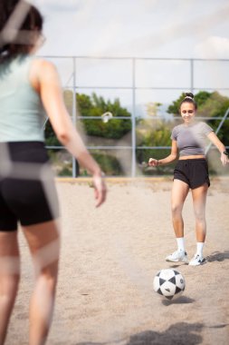 İki kişi açık bir gökyüzünün altındaki bir sahada futbol oynuyor. Biri topa vururken diğeri topu almaya hazırlanıyor. Eğlenceli bir aktivite ve egzersiz içindeler..