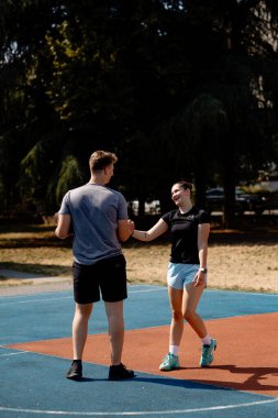 İki basketbol oyuncusu canlı bir kortta dururken dostça bir sohbete girişiyor. Parkta güneşli bir öğleden sonra, takım çalışmalarını ve oyundan keyif aldıklarını vurguluyorlar..