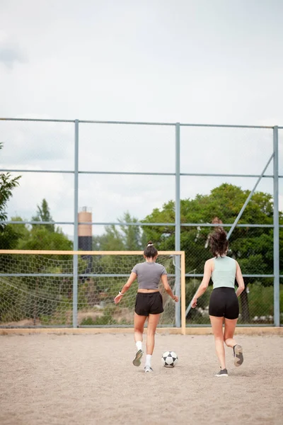 Toprak bir sahada futbol oynayan iki kadın, sıradan bir antrenman sahnesinde topun peşinden koşuyor..