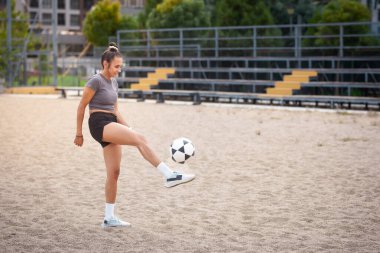 Spor elbiseli genç bir kadın, spor salonunda futbol topunu tekmeliyor. Formda ve odaklanmış..
